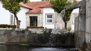 A stone wall with a water feature, a white building with a red-tiled roof, and a tree in the foreground. - Boega Hotel (Vila Nova de Cerveira)