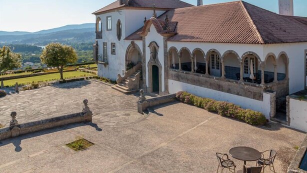 A white building with a tiled roof and arched windows, surrounded by a stone courtyard and a view of distant hills. - Boega Hotel (Vila Nova de Cerveira)