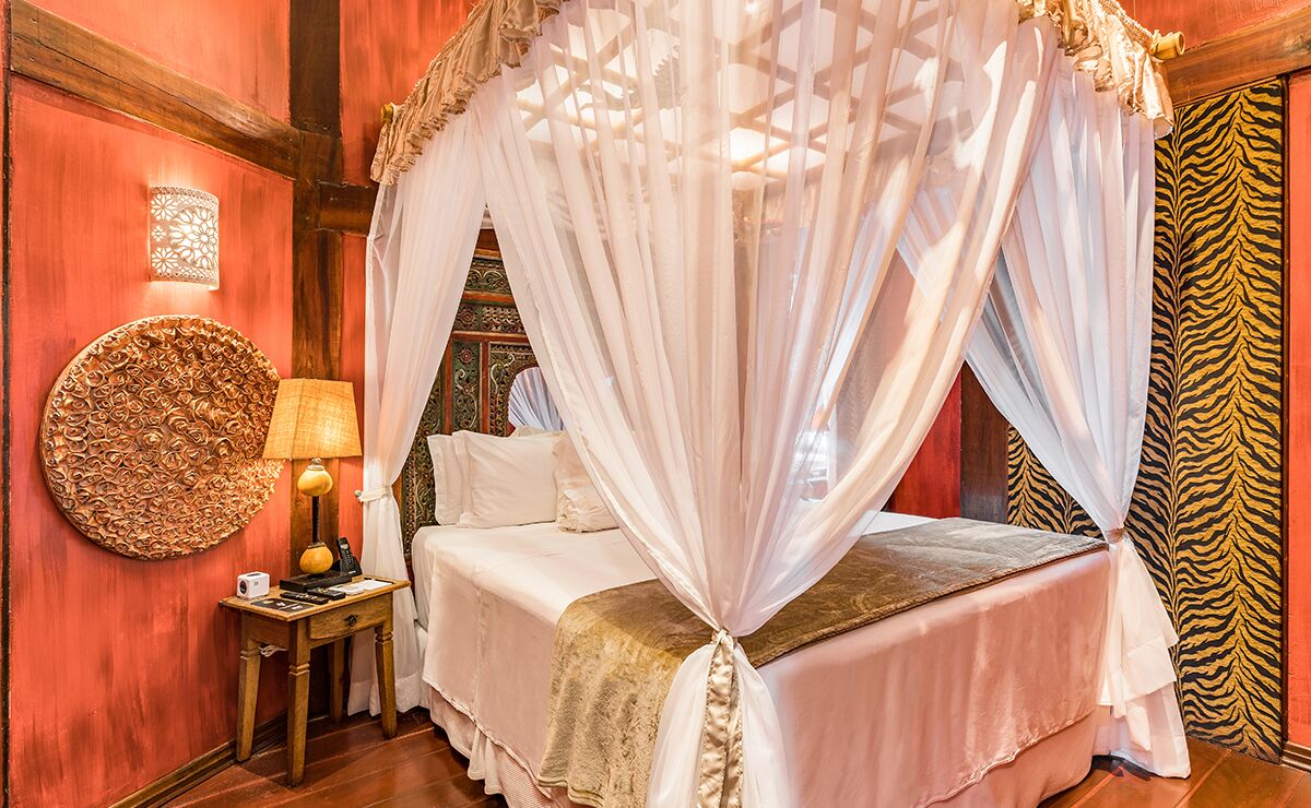 A bed with a canopy, a wall-mounted lamp, and a decorative wall piece.