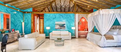 A spacious room with a high ceiling, a bed with a canopy, a sofa, a coffee table, and a painting on the wall.