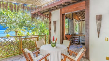 A wooden deck with a round table and chairs, overlooking a beach with palm trees and the ocean.