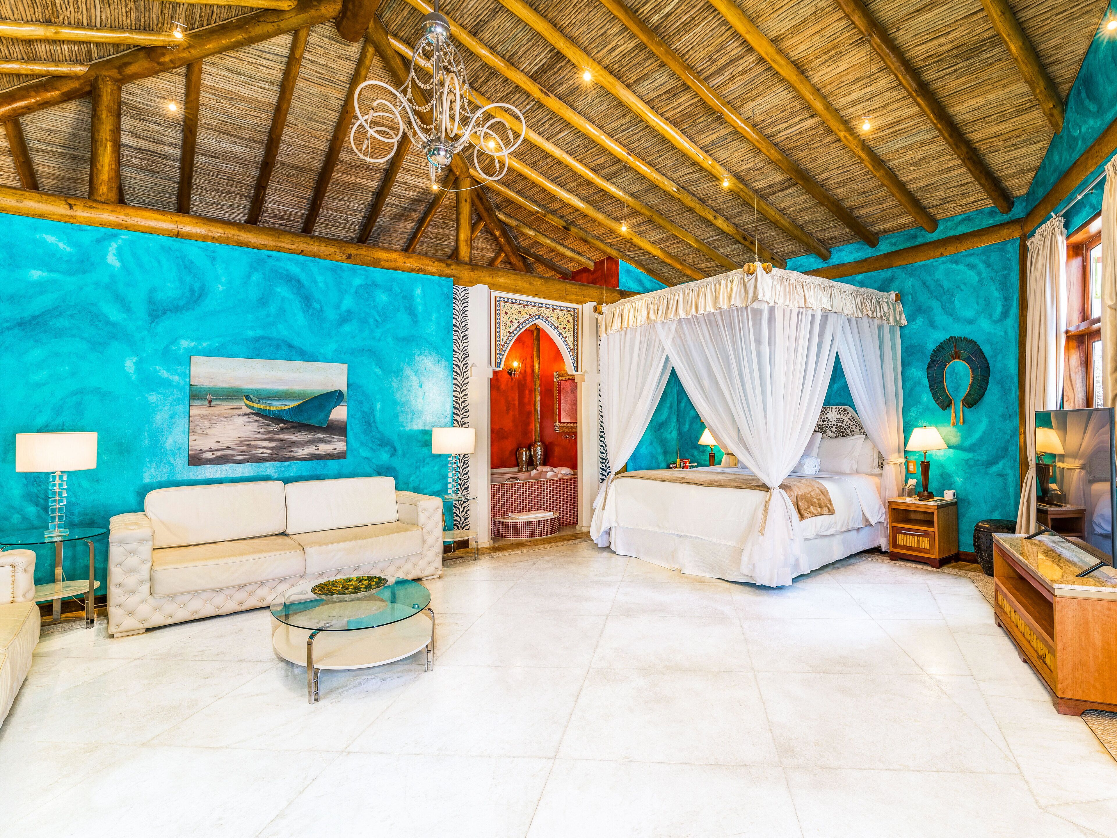 A spacious room with a large bed, a sitting area with a glass coffee table, and a ceiling with exposed wooden beams.
