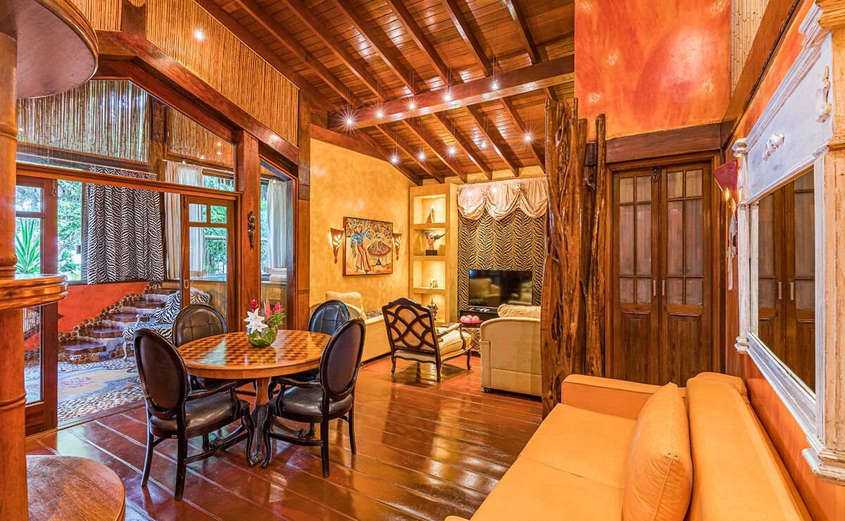 A cozy interior with a wooden ceiling, a dining area with a round table and chairs, a sofa, and a fireplace.