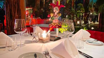 Una mesa de comedor para dos, con un candelabro en el centro, rodeada de plantas tropicales y una figura decorativa.