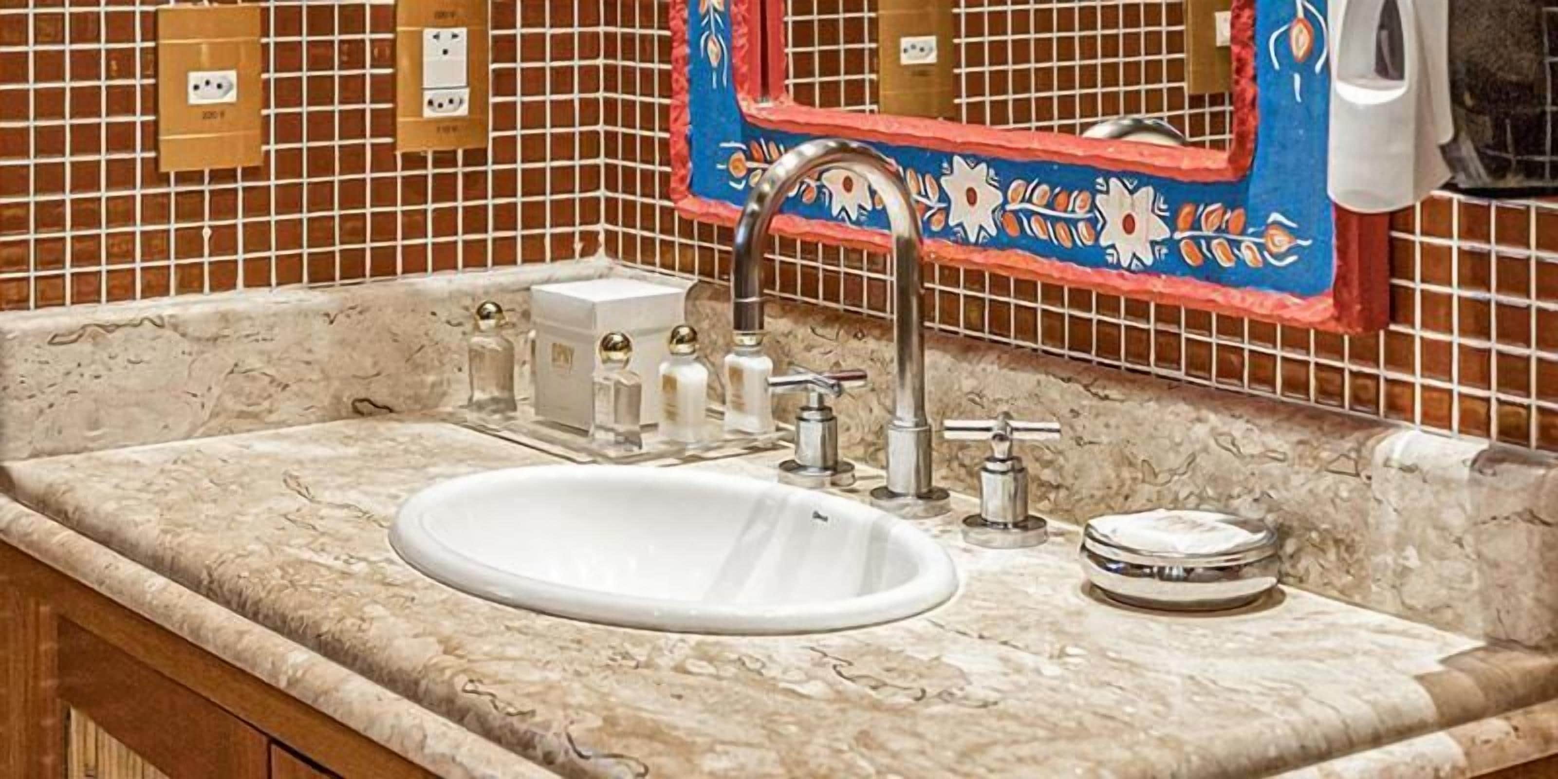 A bathroom with a marble sink, a mirror with a decorative frame, and a tiled wall.