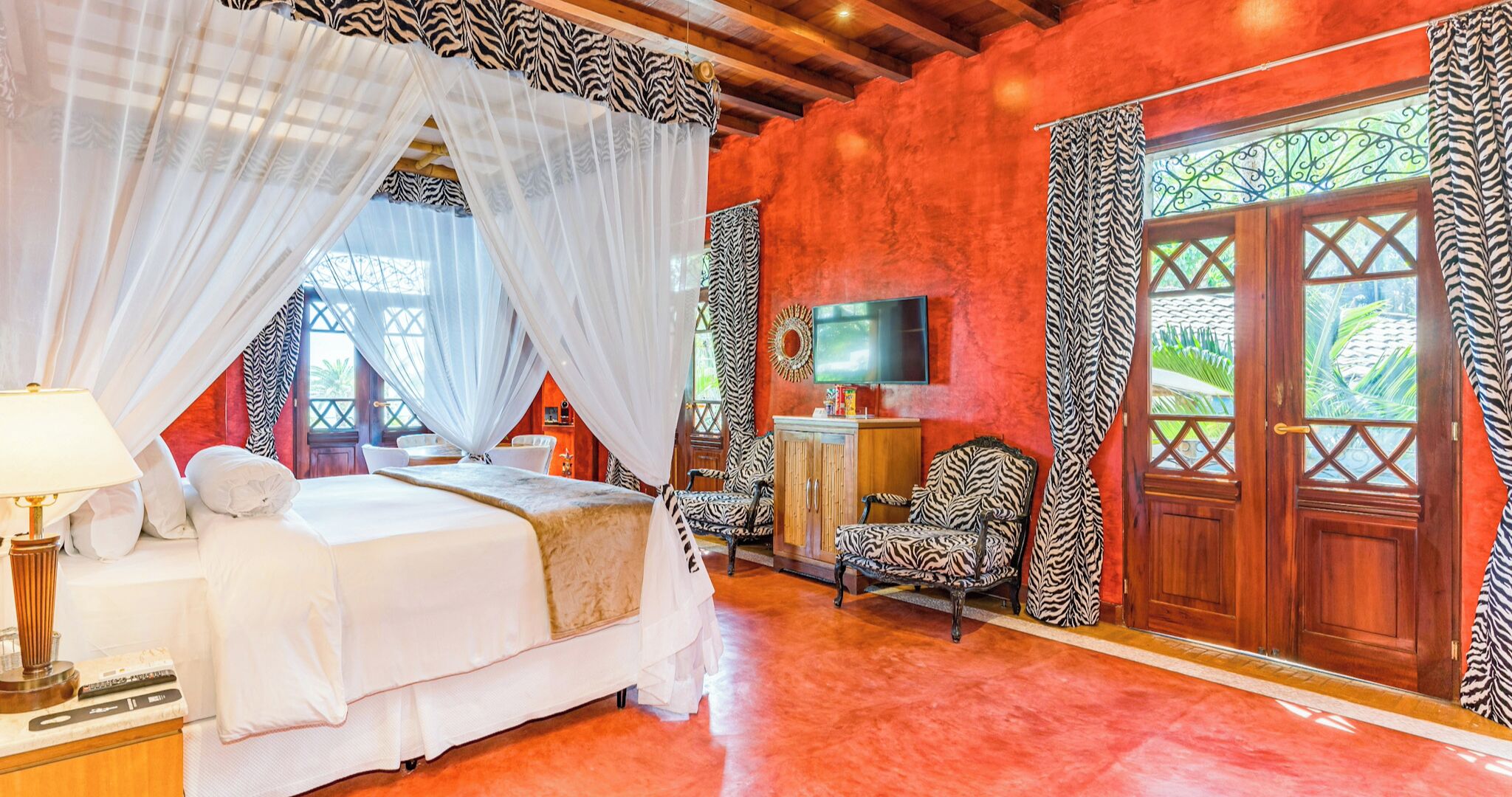 A room with a bed, a TV, a chair, and a window with curtains.