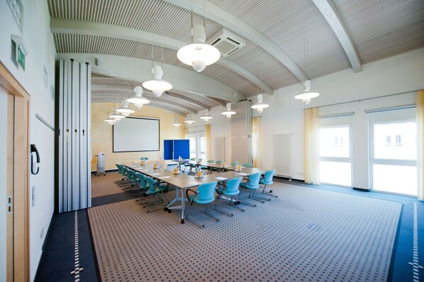 A conference room with a long table, blue chairs, and a projector screen.