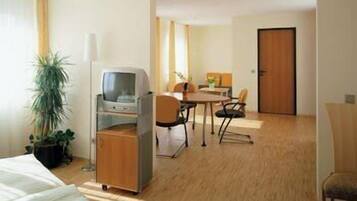 Une chambre d’hôtel comprenant un lit, un bureau avec un ordinateur, une chaise, une petite table et une porte.
