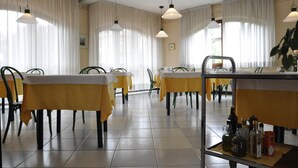 Un espace repas avec des tables recouvertes de nappes jaunes, des chaises, des lampes suspendues et un coin bar avec des bouteilles.