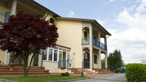 Un bâtiment à deux étages doté d’un balcon, d’une entrée couverte et d’un arbre au premier plan.