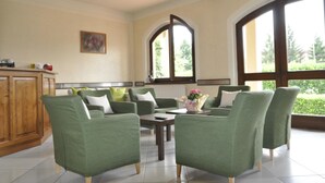 Un salon spacieux avec des fauteuils verts, une table basse et une vue dégagée grâce à de grandes fenêtres.