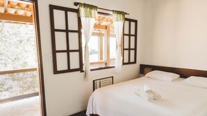 Une chambre d’hôtel avec un lit, des rideaux blancs, une fenêtre donnant sur un paysage agréable et une tête de lit en bois.