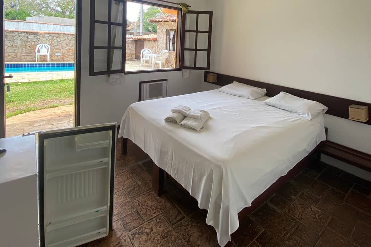 A hotel room with a bed, a small table, a window, and a view of a pool and outdoor seating.