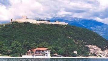 A coastal building with a red roof, situated on a hill with a view of a castle in the background.