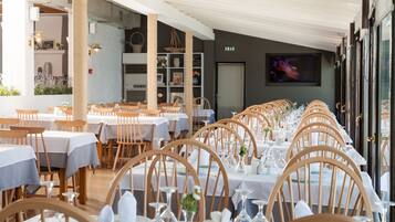 A restaurant with long tables, wooden chairs, and white tablecloths.