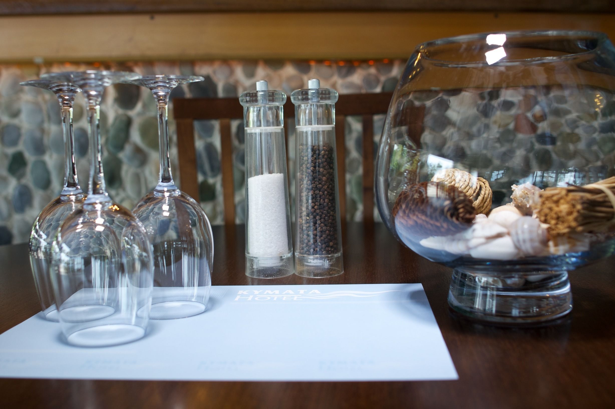 A table with wine glasses, salt and pepper shakers, and a decorative bowl with natural elements.