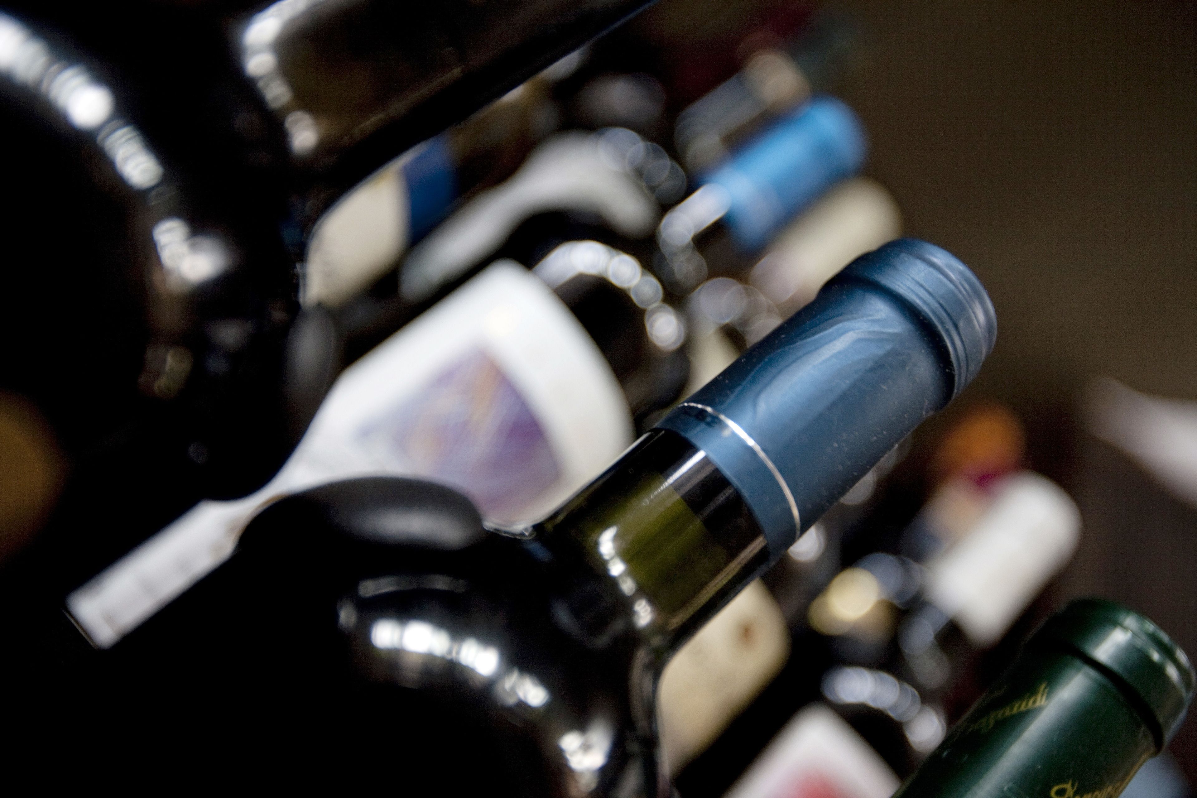Primer plano de varias botellas de vino con etiquetas, algunas con texto visible y otras con el texto borroso.