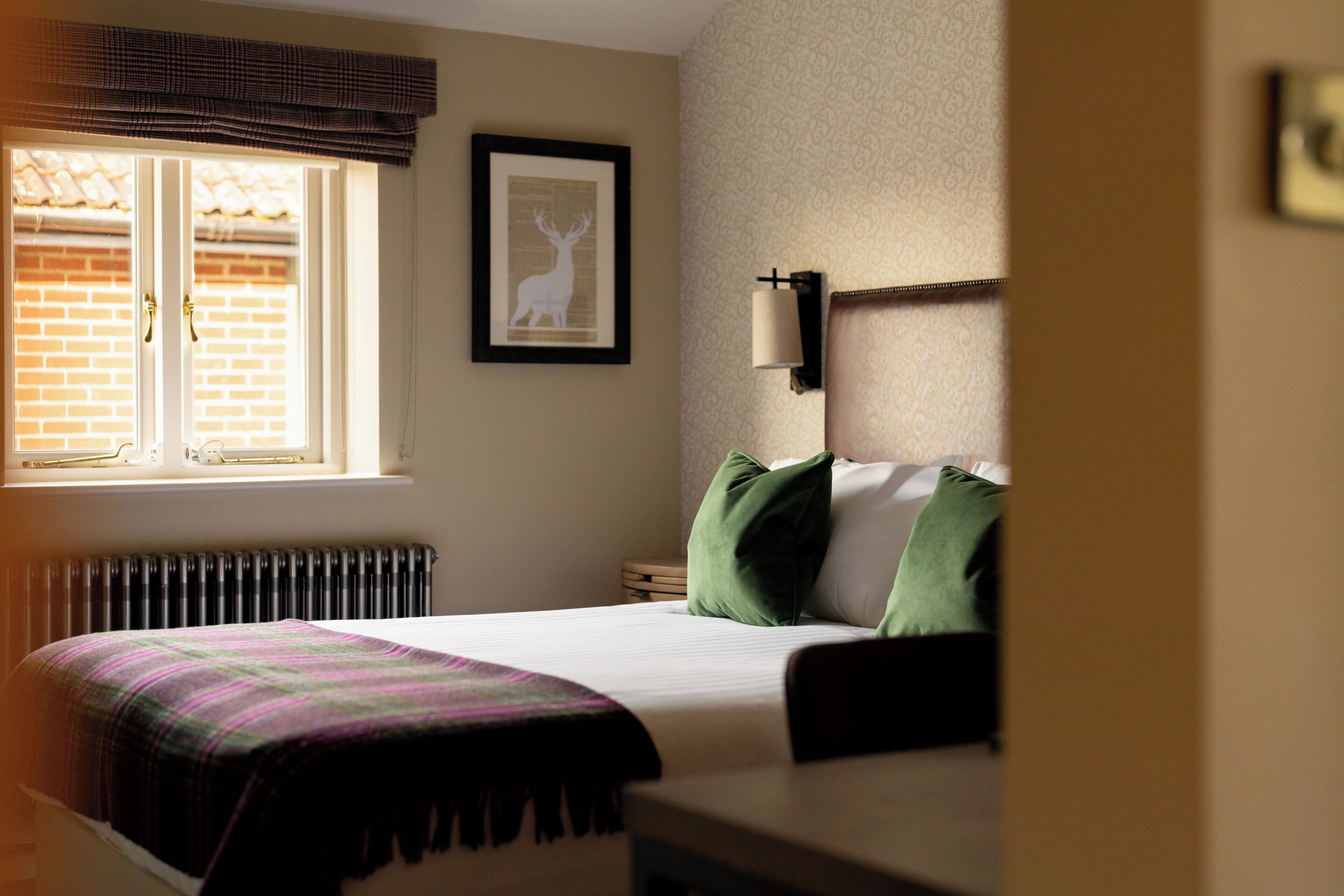 A hotel room with a bed, a window with a view of a brick wall, a radiator, and a framed picture on the wall.