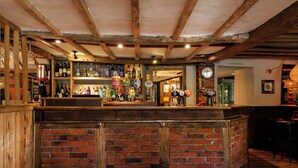 Un espace bar avec un comptoir en briques, des poutres en bois et une variété de bouteilles et de verres.