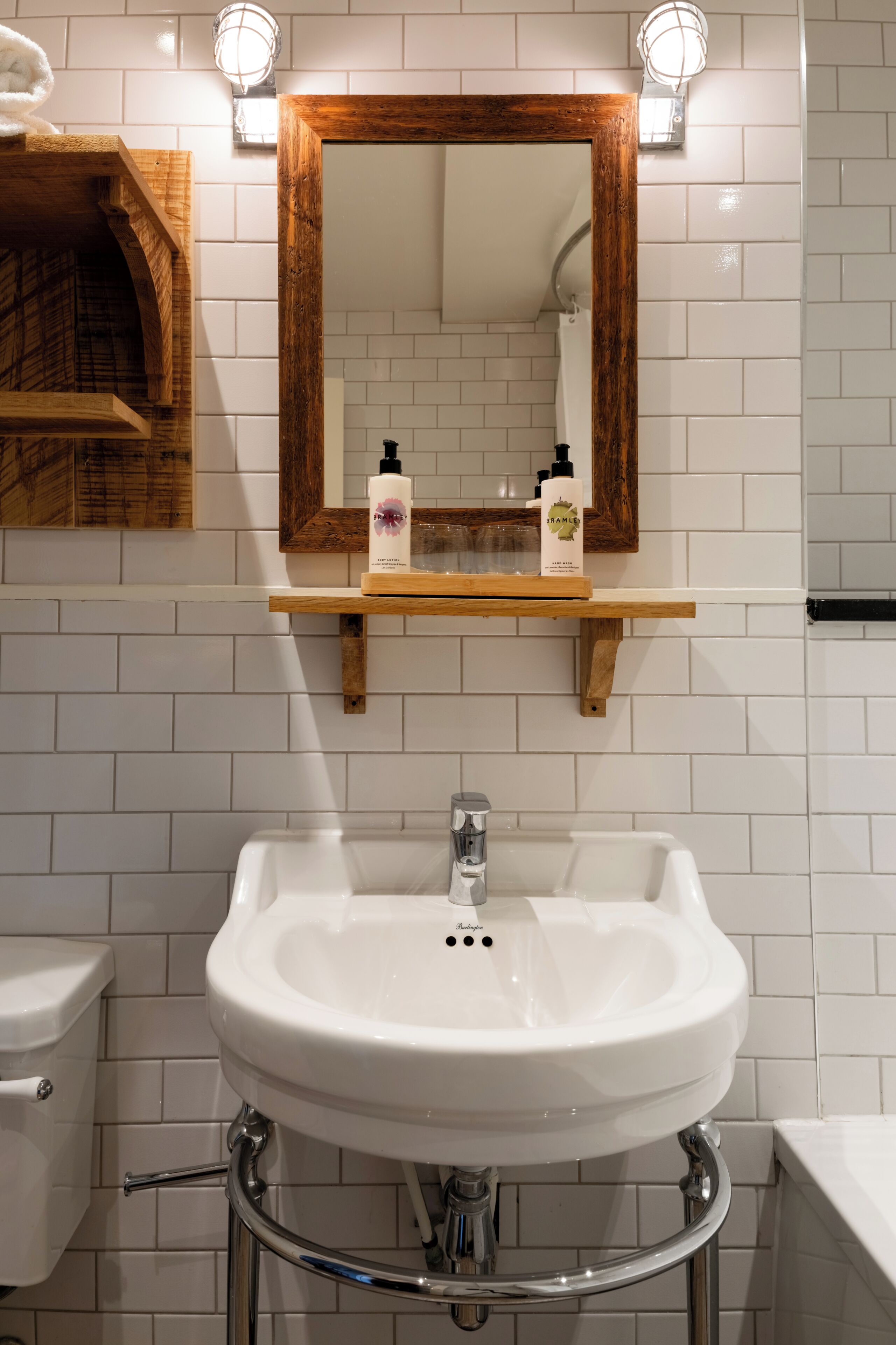 A bathroom with a white sink, a wooden-framed mirror, and a shelf with toiletries.