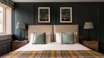 A bedroom with a large bed, two bedside tables, a window with curtains, and two framed pictures on the wall.