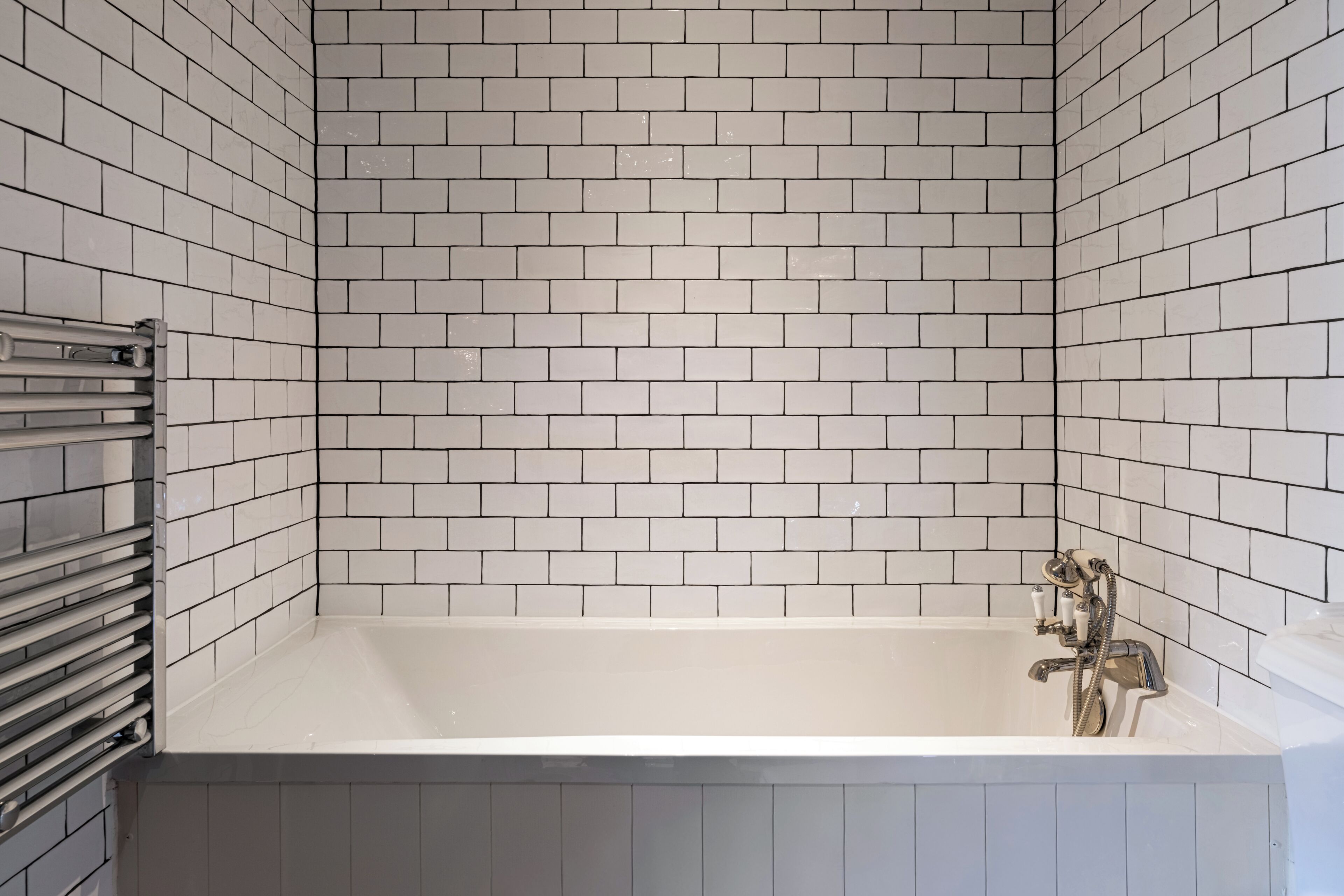 A bathroom with white tiled walls, a bathtub, and a towel rack.