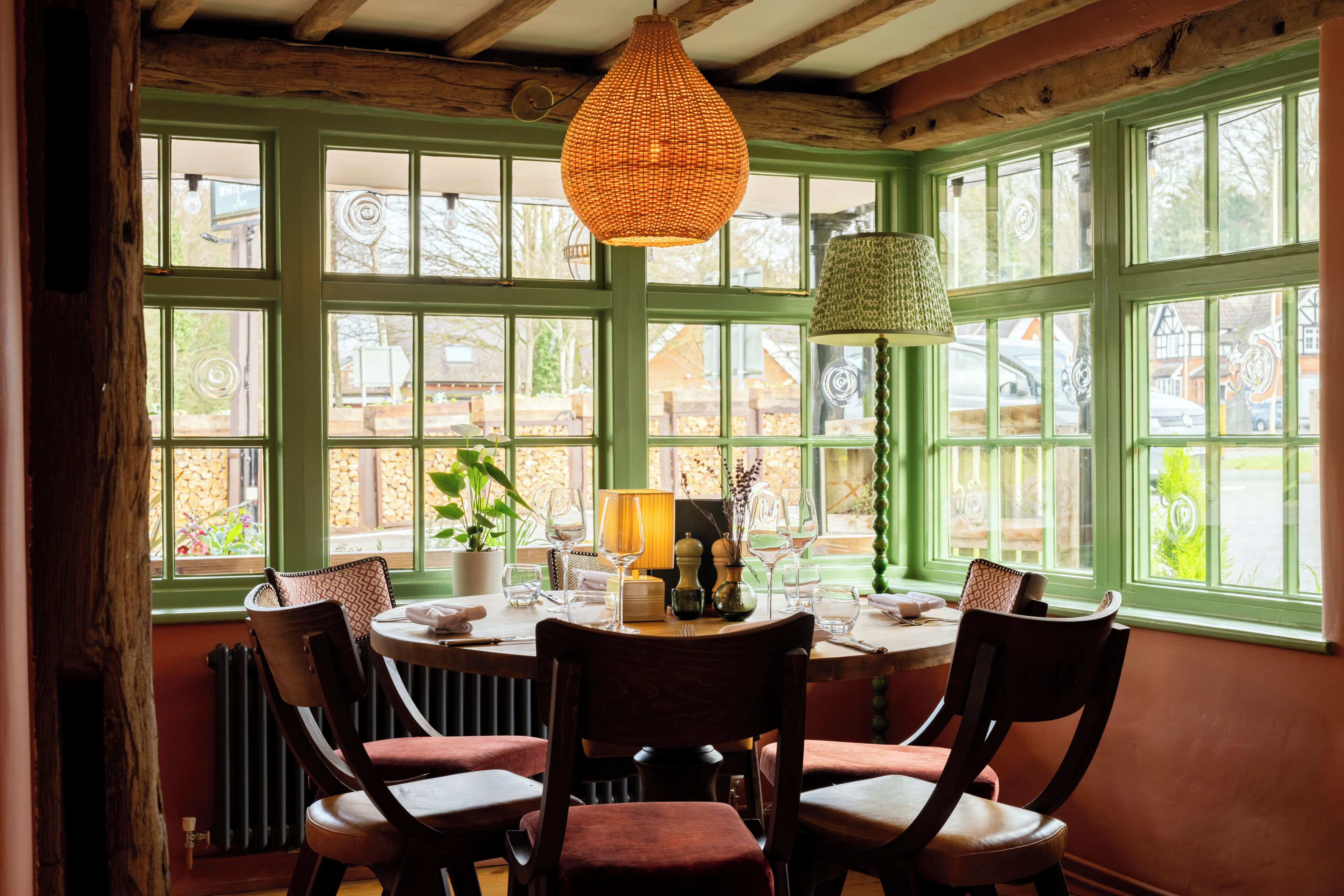 A dining area with a table set for four, surrounded by chairs, large windows, and a hanging light fixture.