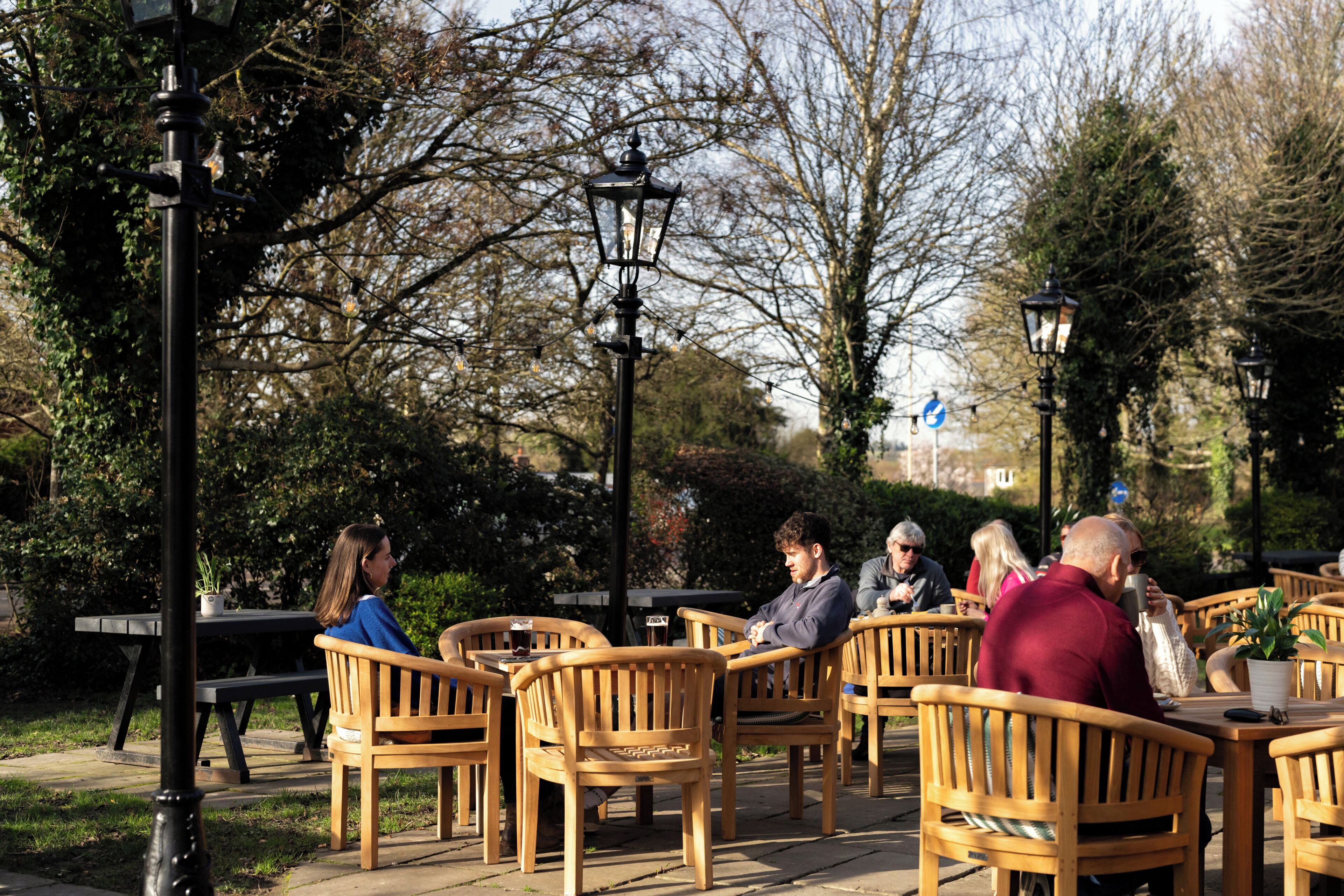A courtyard with wooden tables and chairs, surrounded by trees and lamp posts.