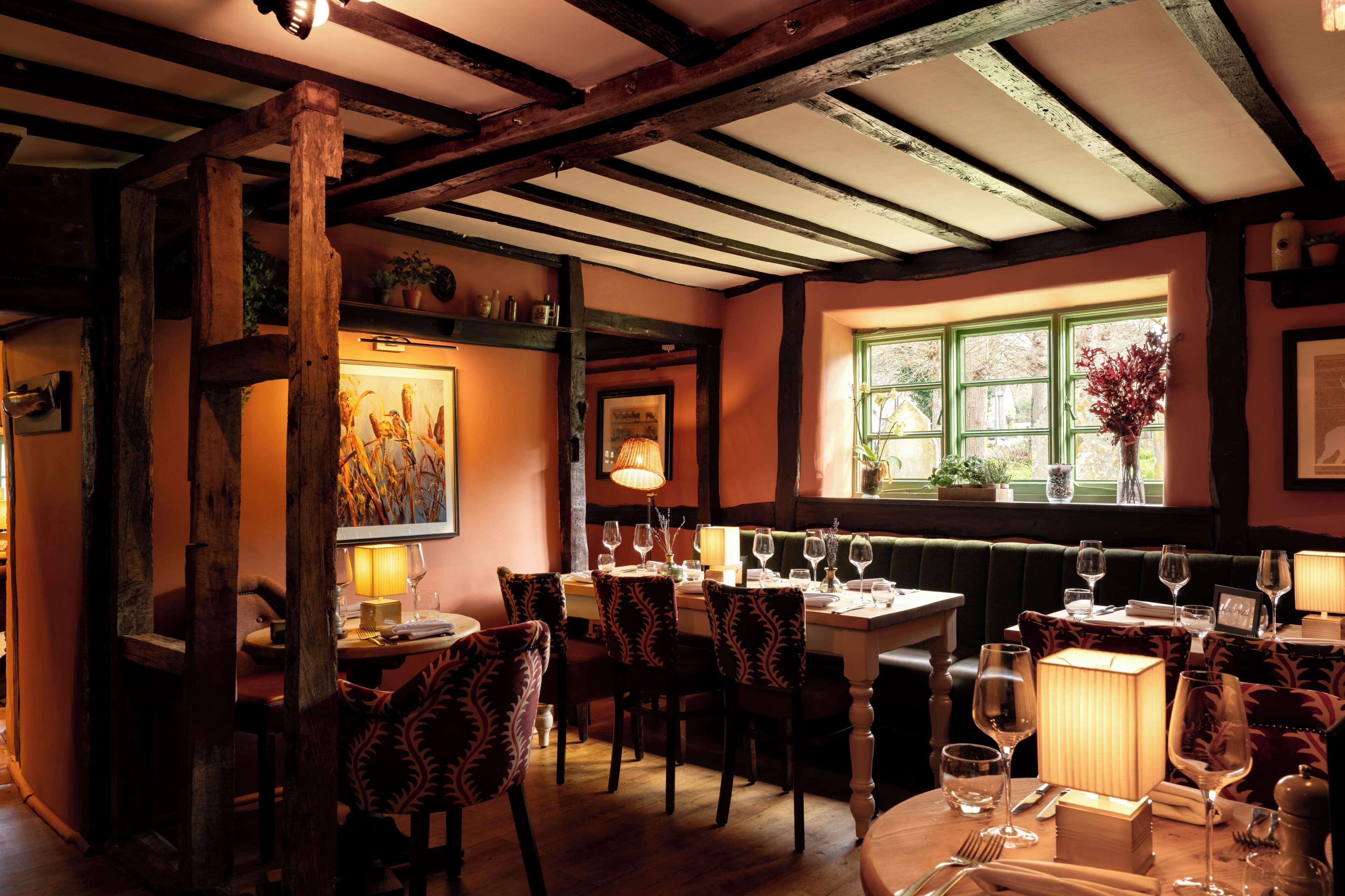 A dining area with wooden beams, green window frames, and a table set for dining.