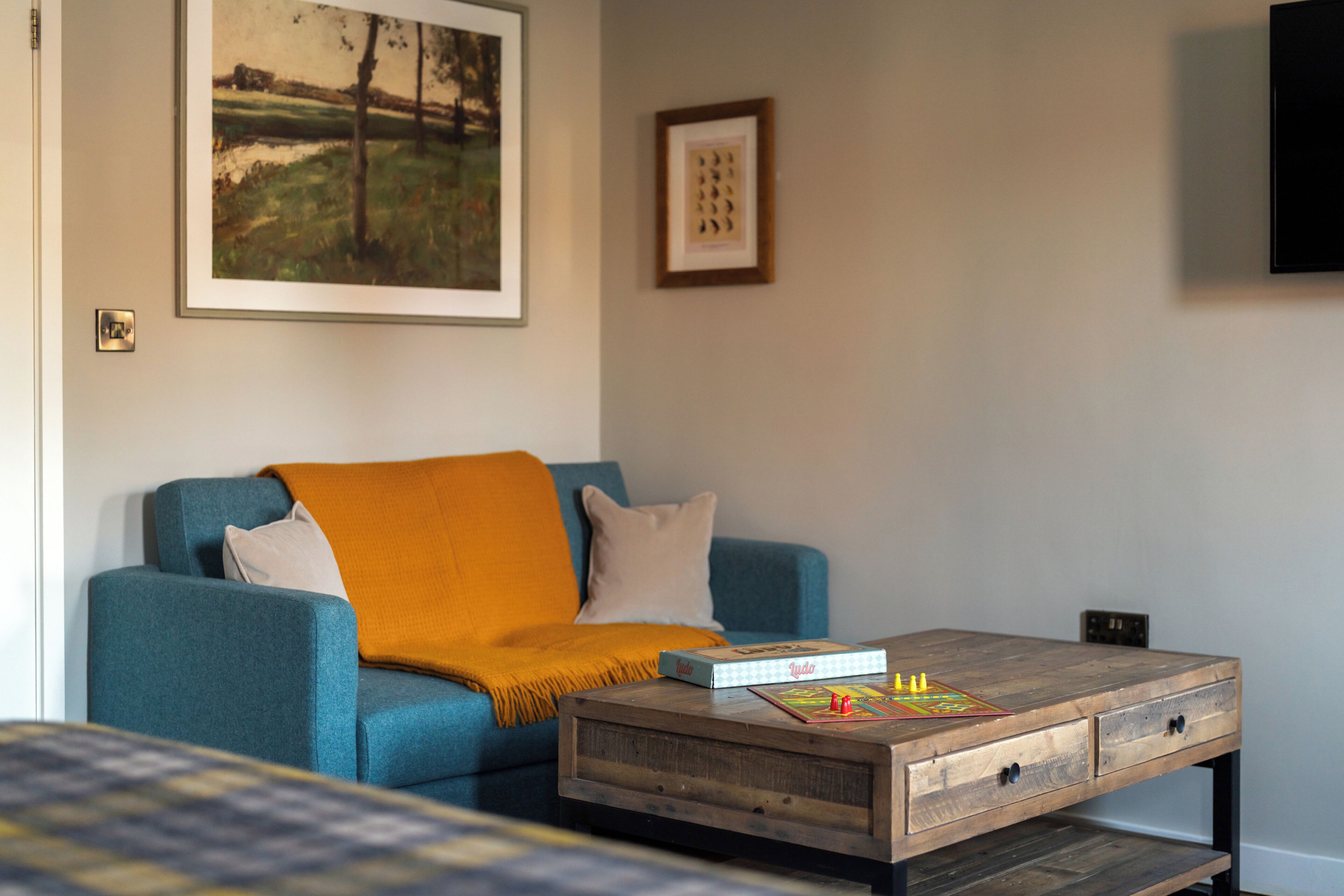 A living room with a blue sofa, a coffee table with a board game, a painting on the wall, and a television.