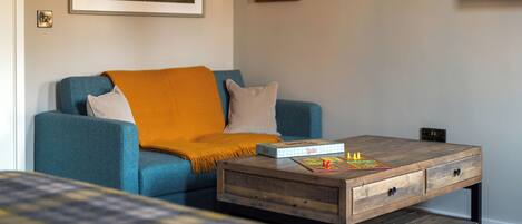 A living room with a blue sofa, a coffee table with a board game, a painting on the wall, and a television.