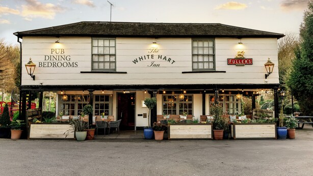 Un pub avec une enseigne indiquant « The White Hart Inn », des tables à l’extérieur et des plantes en pot.