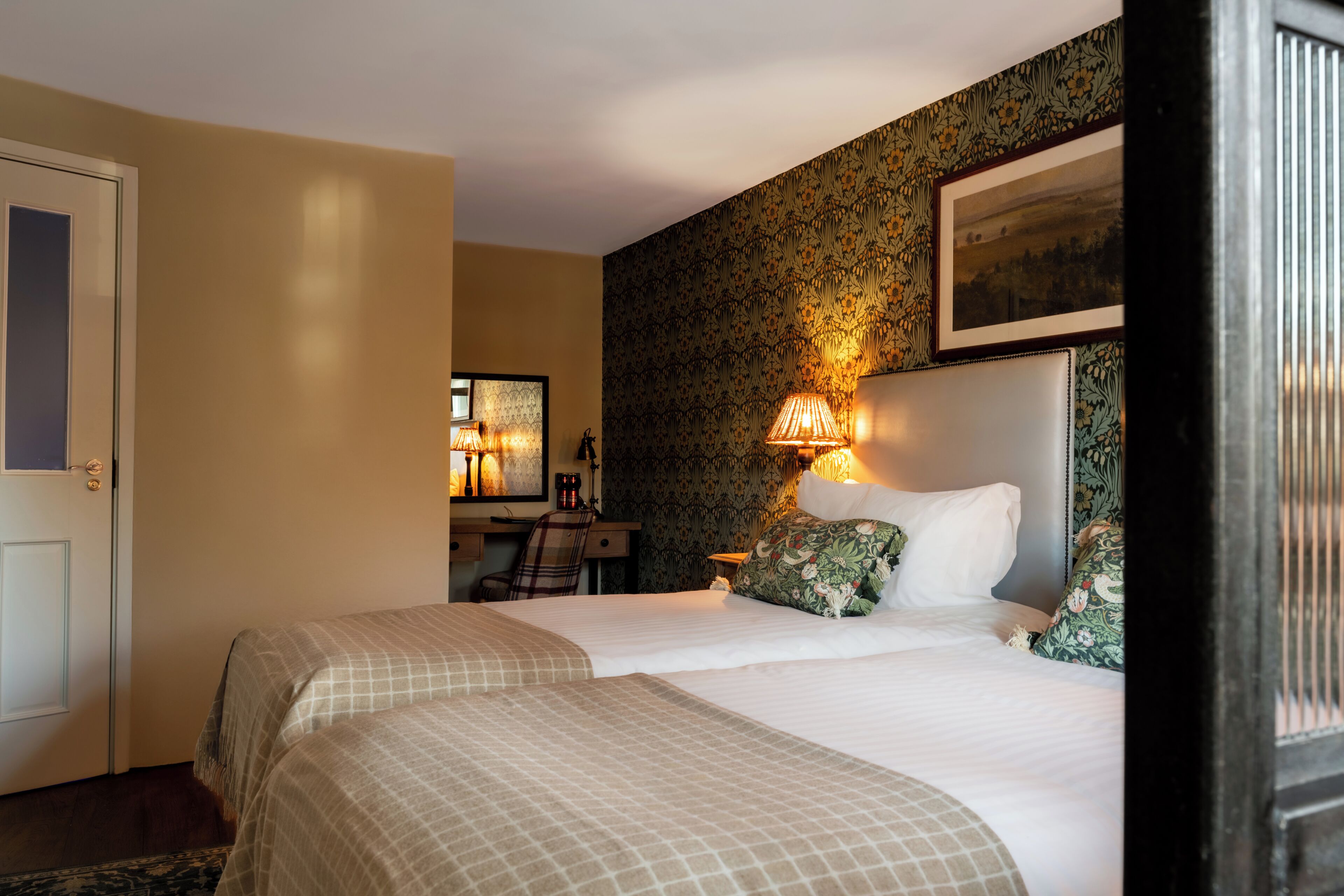 A hotel room with two beds, a desk, a chair, and a desk lamp.