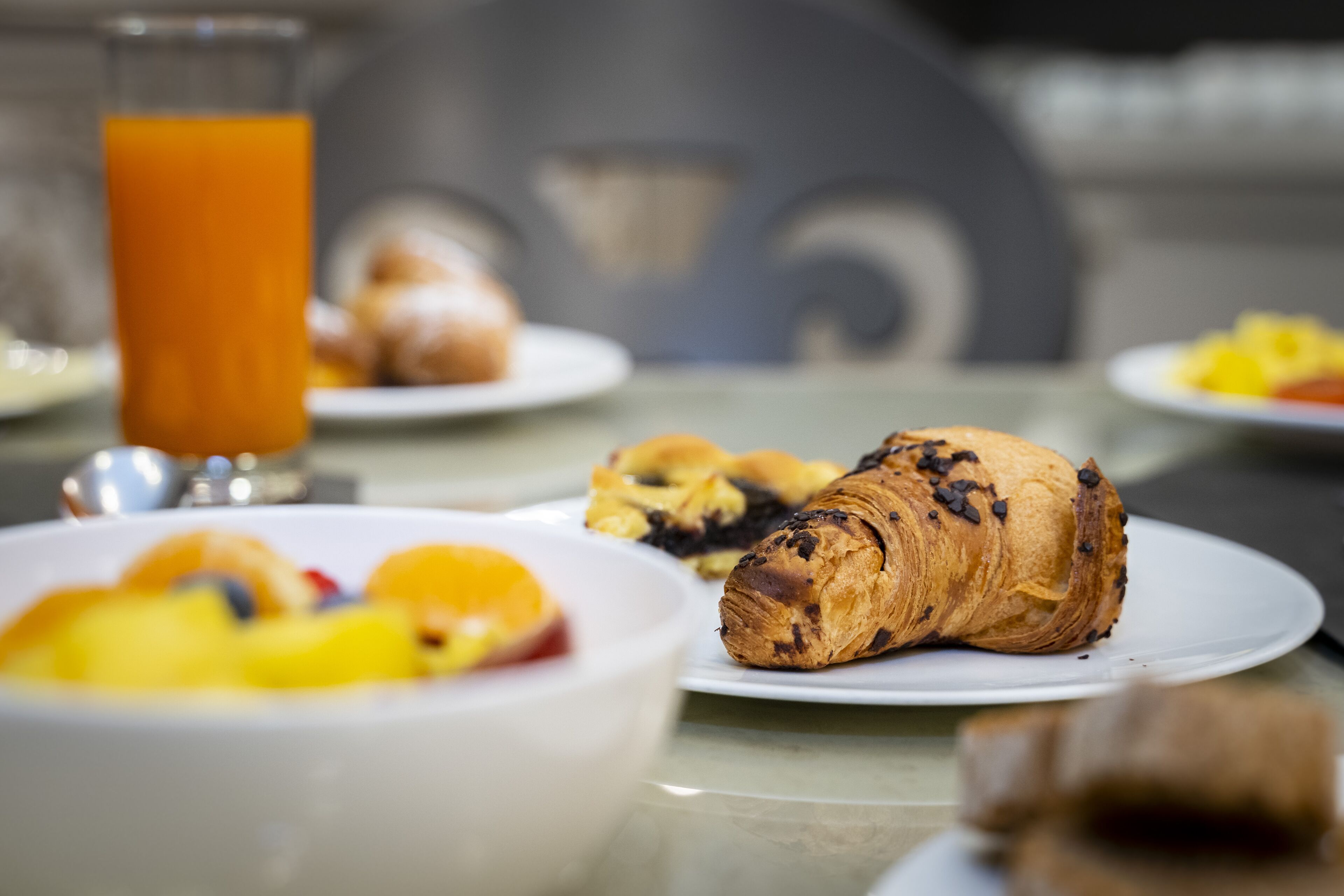 A breakfast setting with croissants, fruit, and a glass of orange juice on a table.