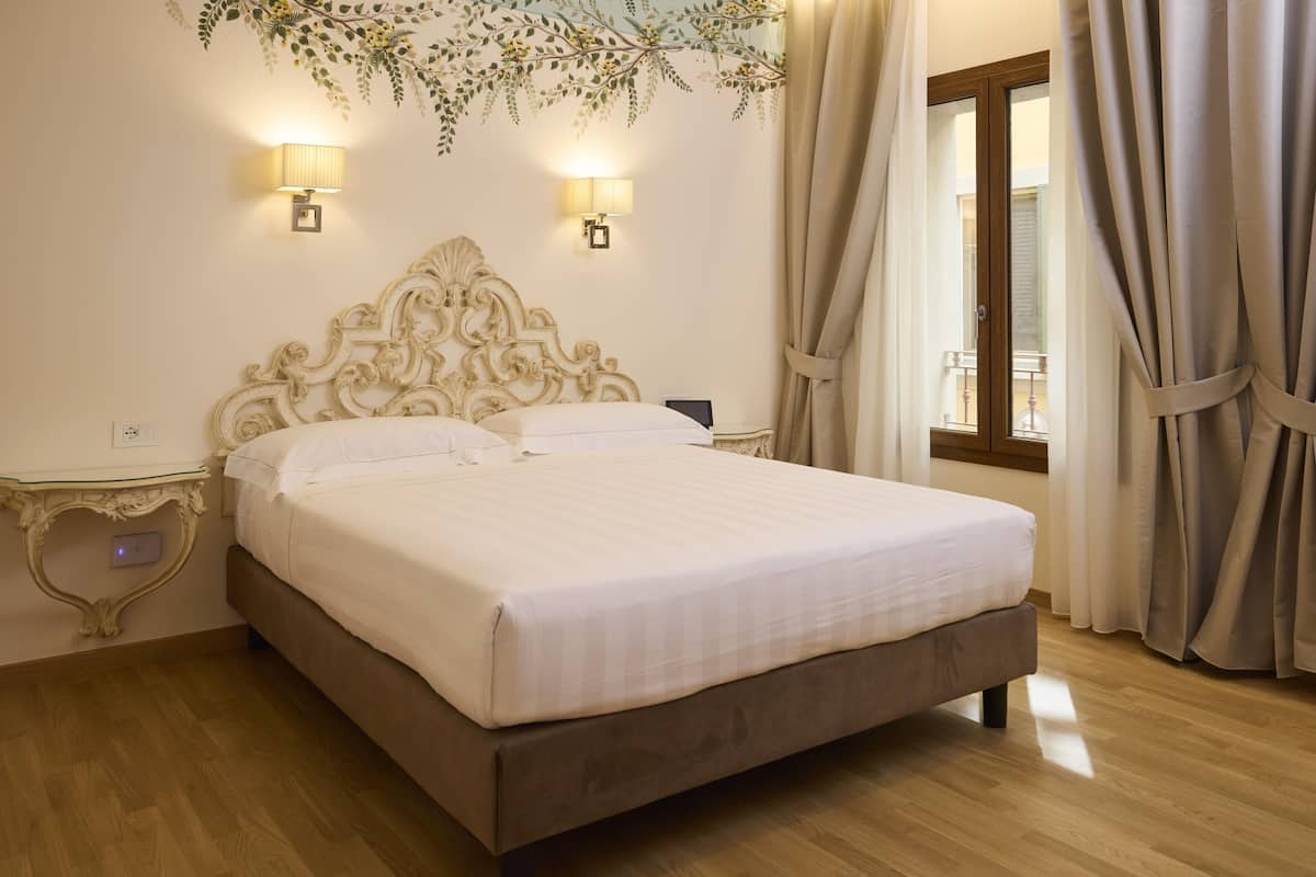 A neatly made bed with a wooden headboard, two wall-mounted lamps, and a window with curtains.