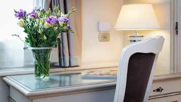 A desk with a vase of flowers, a lamp, and a chair.