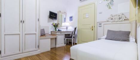 Una habitación de hotel con cama, escritorio, silla, armario y aire acondicionado.