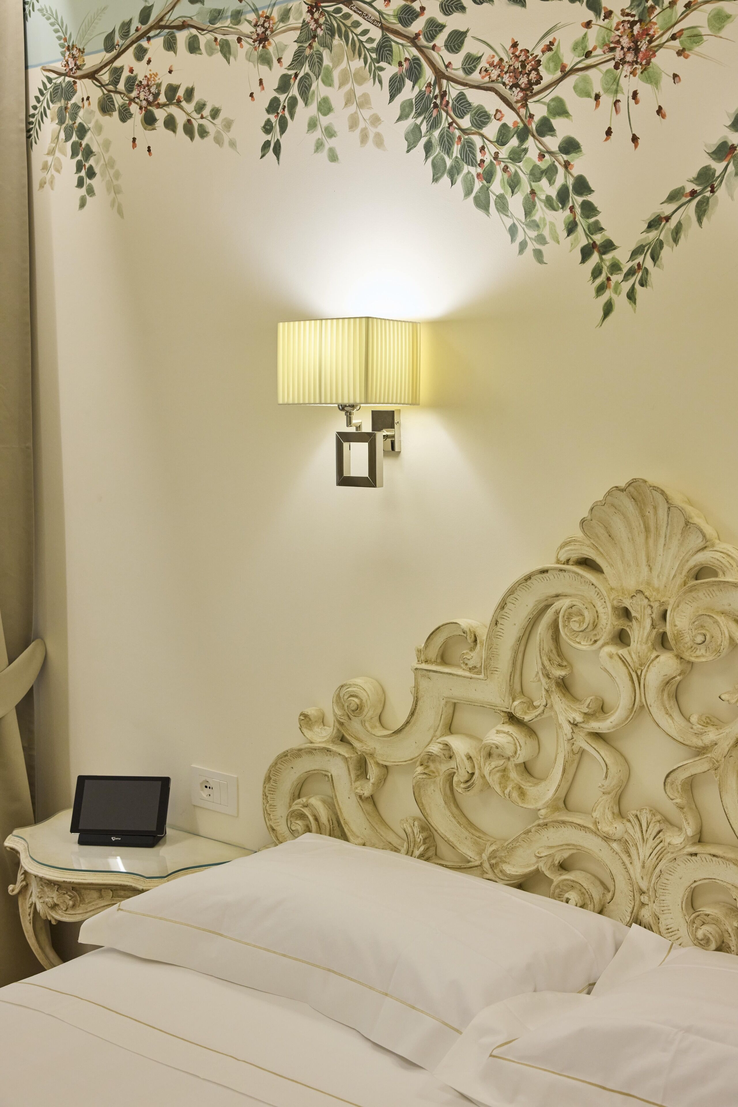 Una habitación de hotel con una cama, una mesita de noche con una lámpara y un mural decorativo en la pared.
