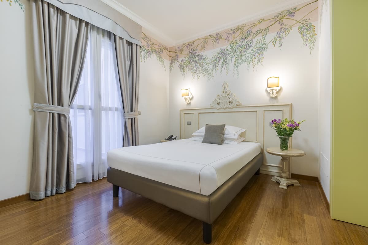 A neatly arranged bedroom with a large bed, a bedside table with a lamp, and a decorative wall hanging.
