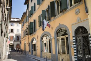 A street view with a building featuring arched windows and a flag. - Art Atelier - Place of Charme (Florence)