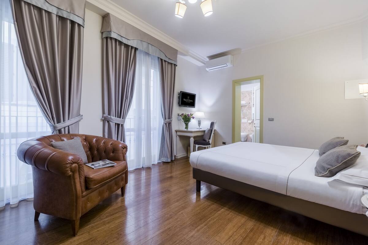 A hotel room with a bed, a leather armchair, a desk, and a television.