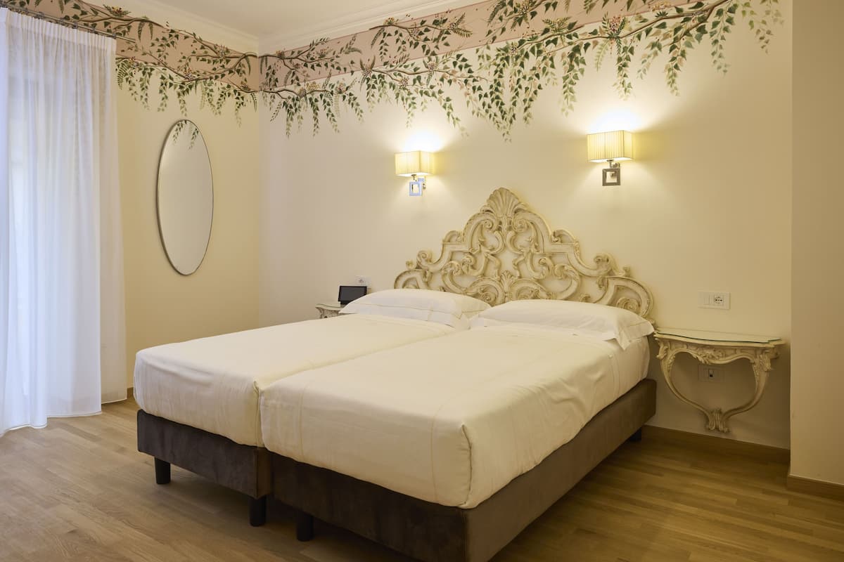 A double bed with a wooden headboard, two bedside tables, a mirror, and a decorative wall hanging.