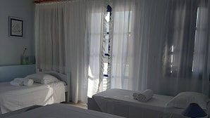 A hotel room with two beds, a ceiling fan, an air conditioning unit, and a window with sheer curtains. - Nefeli Villa (Santorini)