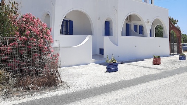 A white building with multiple arches and blue accents, featuring a gravel driveway and potted plants. - Nefeli Villa (Santorini)