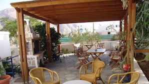 An outdoor patio with wicker furniture, a stone floor, and a wooden pergola. - Nefeli Villa (Santorini)