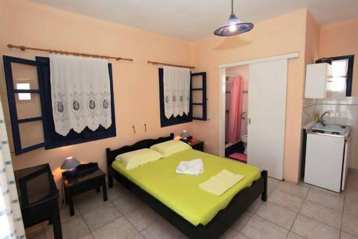 A bedroom with a bed, bedside tables, a desk, a chair, a wardrobe, and a kitchenette.