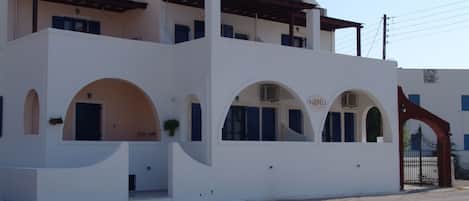 A two-story building with a white facade, multiple arched windows, and a gated entrance.
