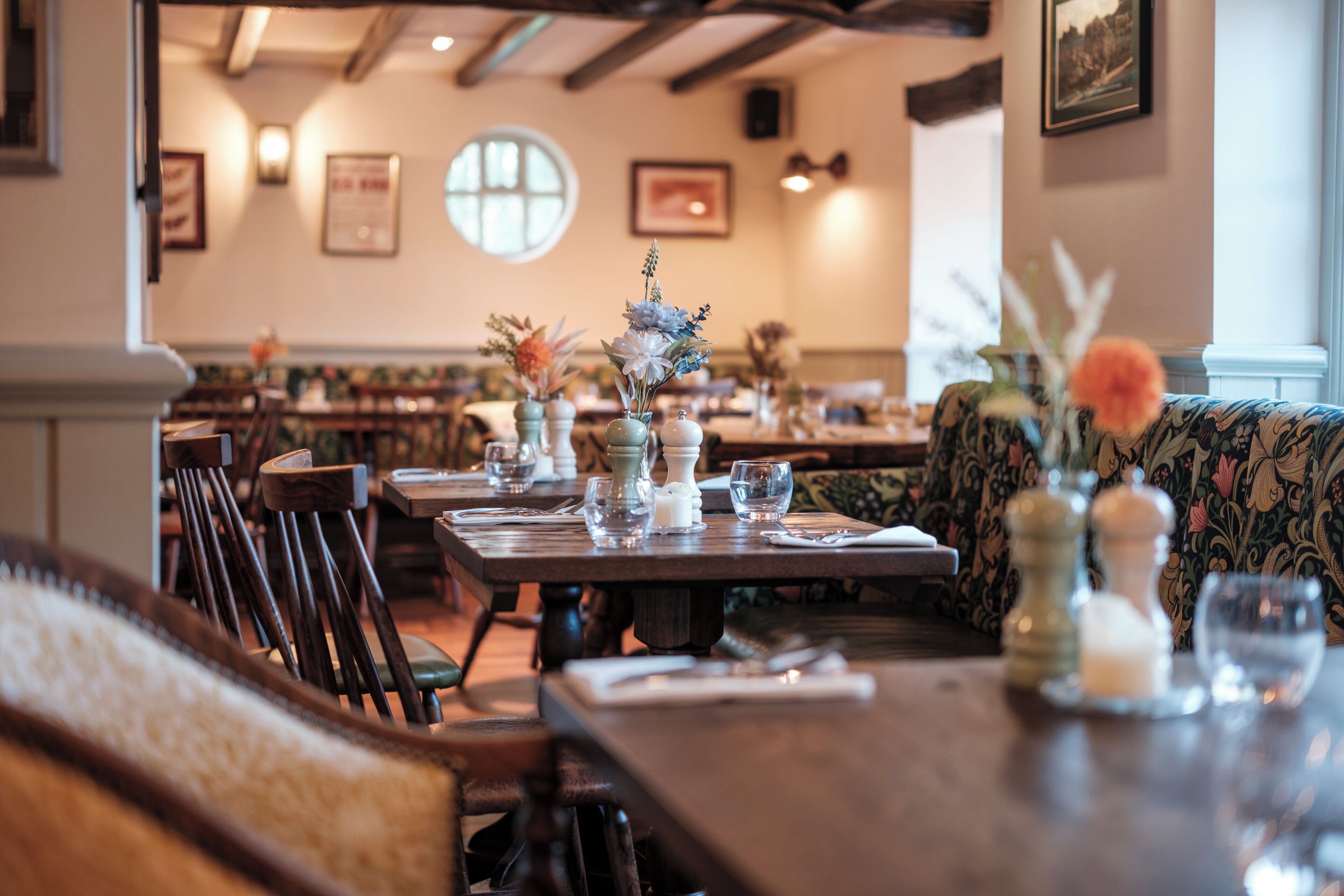 Un interior de restaurante con mesas y sillas de madera, y centros de mesa florales.