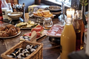 A table with various food items, including croissants, cheese, watermelon, and meat. There are also condiments and a candle in the background.
