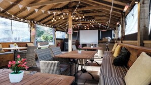 An outdoor seating area with wooden tables and wicker chairs, a whiteboard, and a view of the outdoors.